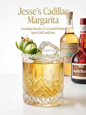 A glass of liquid with a lime garnish and a bottle of liquor.