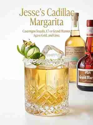 A glass of liquid with a lime garnish and a bottle of liquor.