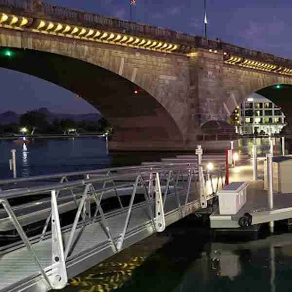 London Bridge, Lake Havasu City, illuminated at night, spans over water with a dock and a metal gangway in the foreground.