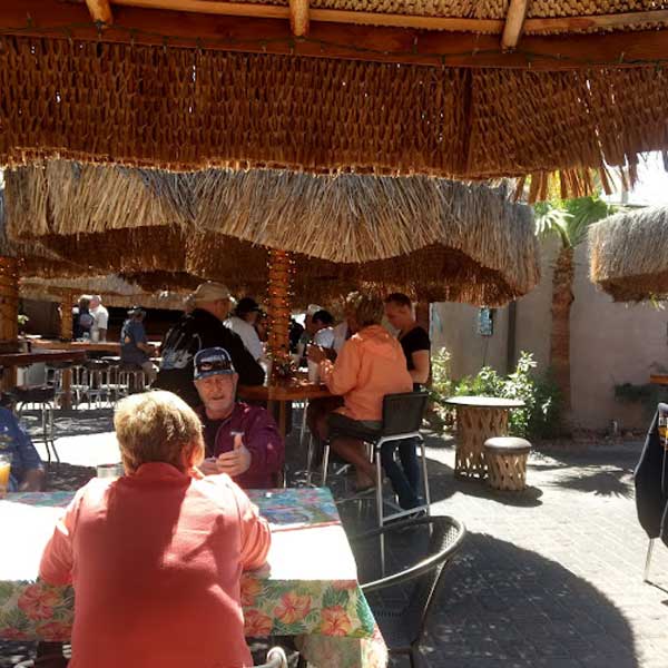 People sitting at tables under thatched umbrellas in an outdoor restaurant on a sunny day.