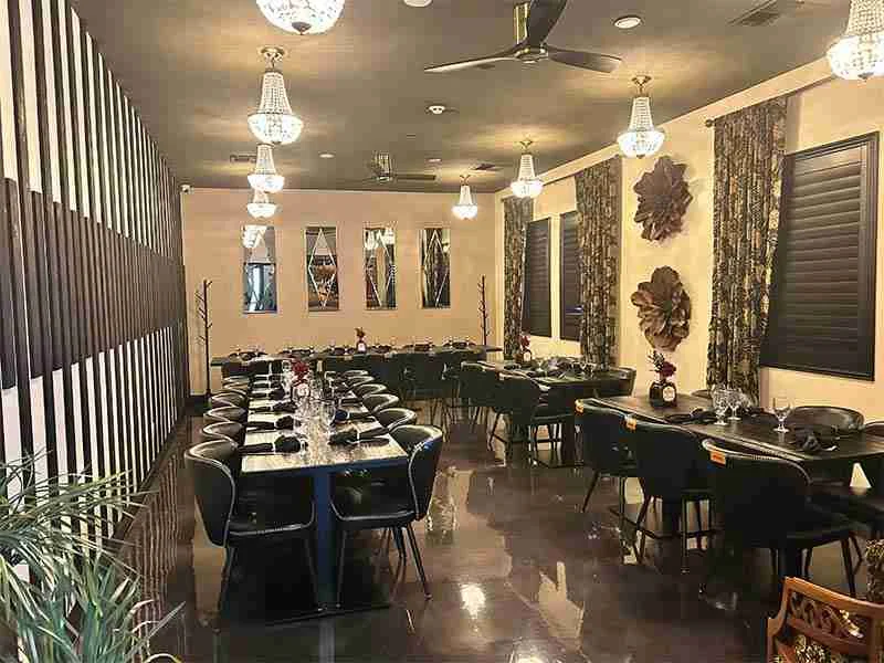 A modern, elegant dining room with black tables and chairs, set for guests; crystal chandeliers hang from the ceiling, and decorative wall elements add style.